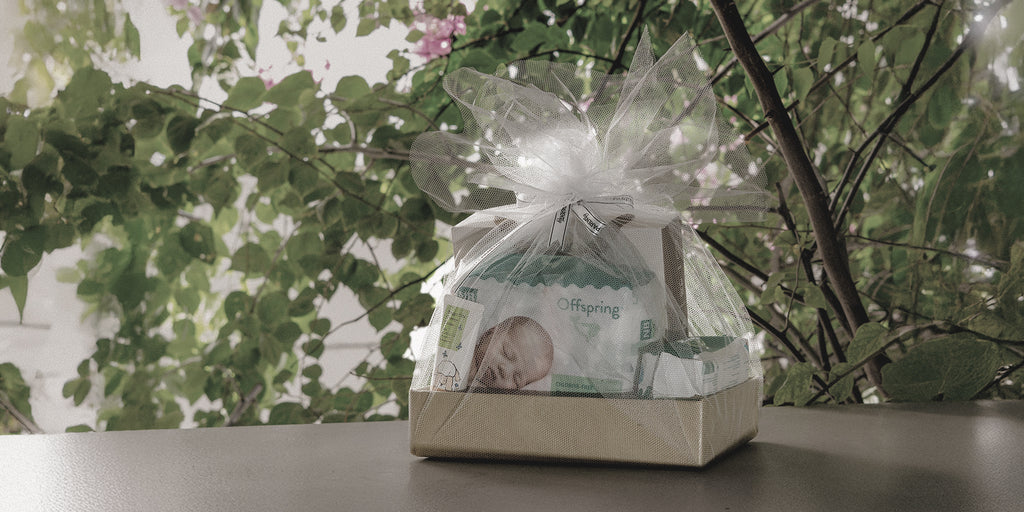 Gift package with a baby photo inside, tied with a ribbon, on a table with a green leafy background