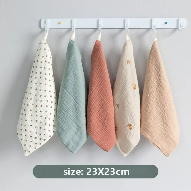 Five colorful baby bibs hanging on a white rack against a gray background.