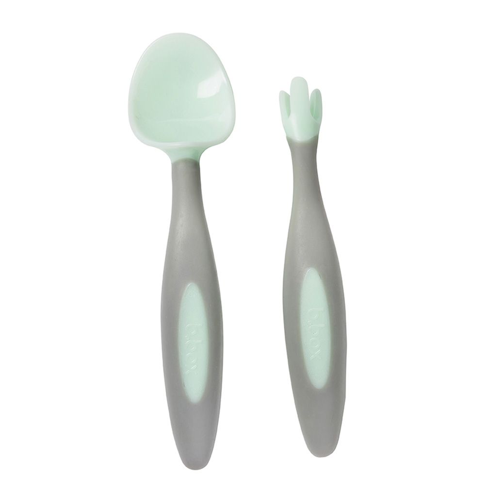 Set of baby spoon and fork with green ends on gray handles against a white background